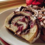 Close-up of a slice of Cherry Chocolate Swirl Rolls showing the sweet cherry filling and chocolate swirl, topped with white icing.