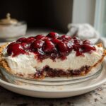 A thick slice of Cherry Coconut Cream Pie showing the graham cracker crust, creamy filling, and cherry topping.