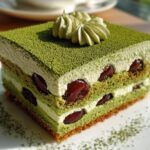 A square slice of layered Cherry Matcha Tiramisu featuring green cake, white cream, and dark cherries.