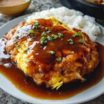 A plate of Chicken Egg Foo Young smothered in thick garlic gravy, served with white rice.