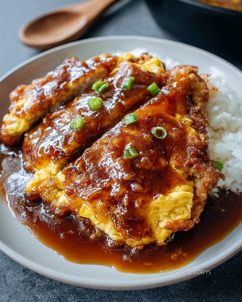 A serving of Chicken Egg Foo Young covered in rich garlic gravy, served over white rice and garnished with scallions.