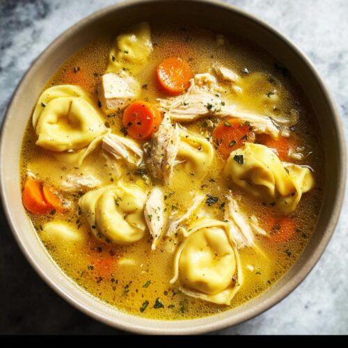 Overhead close-up of a bowl of Chicken Tortellini Dinner Soup featuring shredded chicken, sliced carrots, and herbs in a rich broth.