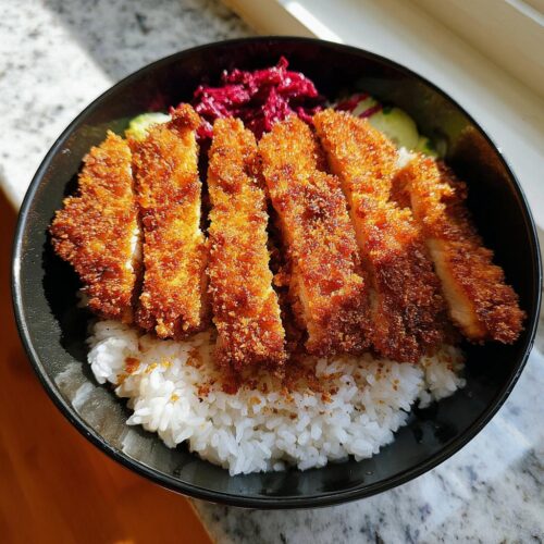 A close-up of a Classic Chicken Katsu Rice Bowl featuring sliced, crispy fried chicken over white rice with pickled vegetables.