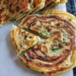 Close-up of freshly pan-fried Classic Scallion Pancakes, sliced into wedges, showing flaky layers and green scallions.