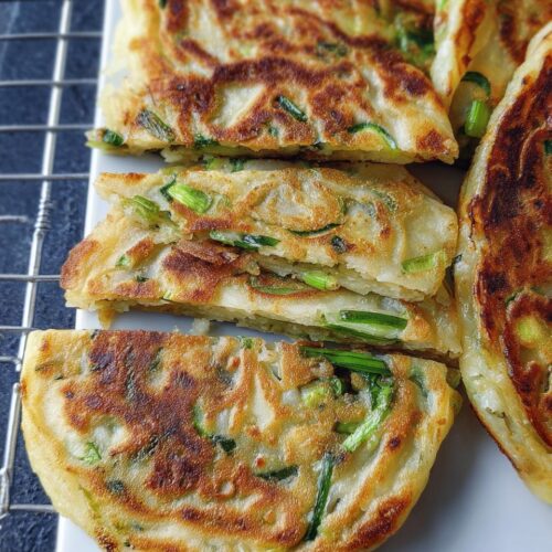 Close-up of flaky, pan-fried Classic Scallion Pancakes cut into wedges, showing layers and green scallions.