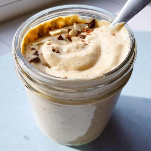 Close-up of thick, creamy blended vanilla overnight oats topped with chocolate shavings in a glass jar.