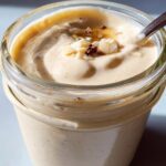 Close-up of creamy blended vanilla overnight oats topped with nuts and drizzled honey in a glass jar.