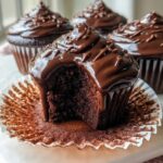Close-up of a Cupid’s Chocolate Cupcake with a bite taken out, showing moist interior and dripping chocolate ganache.