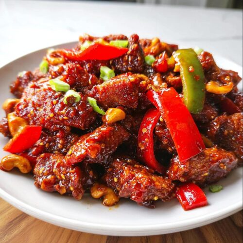 A close-up of glossy, saucy Dragon Chicken with Bell Peppers, garnished with cashews and green onions.