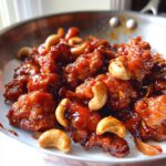 Close-up of glossy, dark red Dragon Chicken with Cashews served in a white bowl or pan.