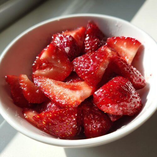 Close-up of glistening, sliced strawberries in a small white bowl, perfect for an Easy Strawberry Snack.