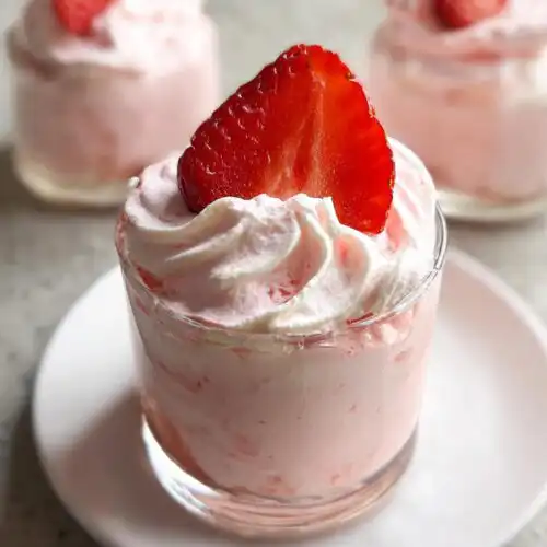 Close-up of a glass serving of Easy Whipped Strawberry Mousse topped with whipped cream and a fresh strawberry slice.
