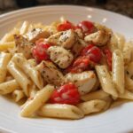 Close-up of a white bowl filled with Family-Friendly Chicken Pasta, featuring penne, seasoned chicken chunks, and halved cherry tomatoes.