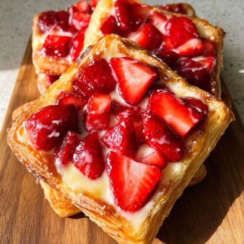 Close-up of a flaky pastry topped with bright red sliced strawberries and a drizzle of white glaze, representing a Fresh Strawberry Danish.