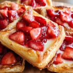 A stack of golden, flaky Fresh Strawberry Danish pastries topped with glazed strawberries and cream cheese filling.
