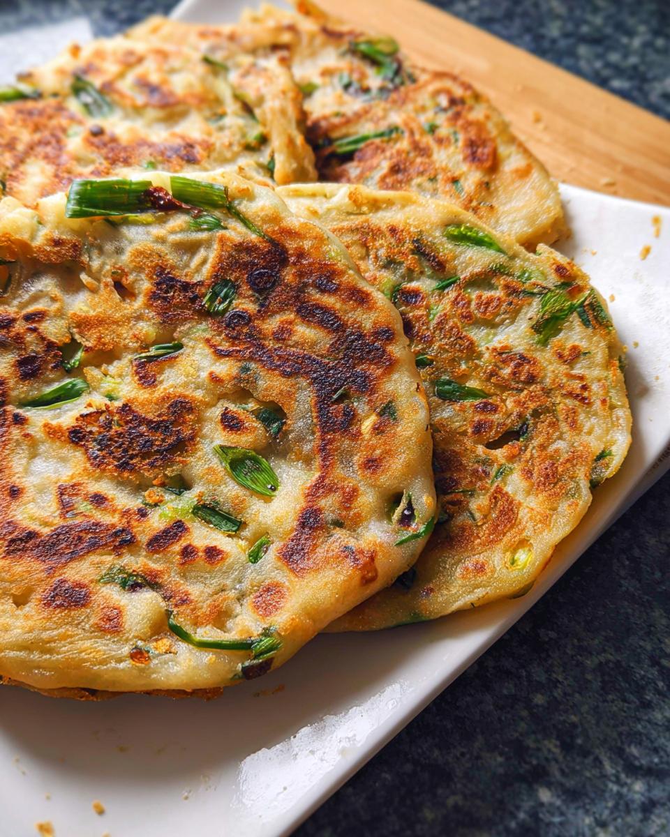 Close-up of several golden-brown Frozen-to-Pan Scallion Pancakes stacked on a white plate.