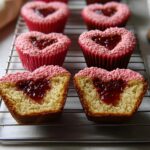 Two halves of a Heart-Filled Valentine Cupcake with Jam Center showing the moist interior and raspberry jam filling, resting on a cooling rack.