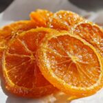Close-up of glistening, bright orange Honey Candied Orange Slices resting on white parchment paper.