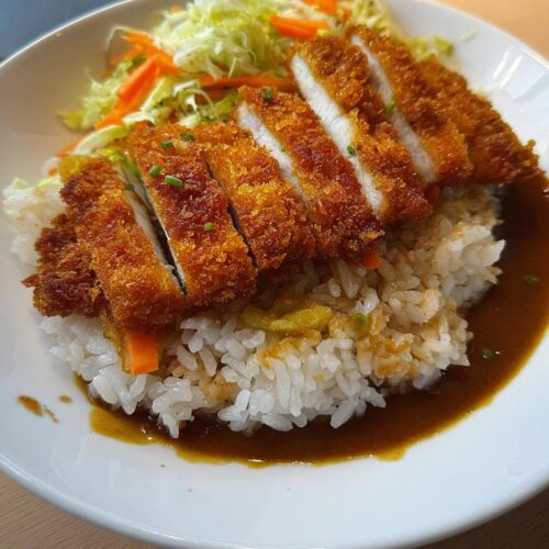 A close-up of a Katsu Bowl with Brown Rice, featuring sliced crispy katsu over rice with curry sauce and shredded cabbage salad.