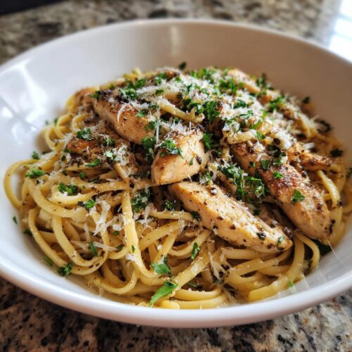 A white bowl filled with Light Garlic Chicken Pasta, topped with sliced chicken breast, grated Parmesan, and fresh parsley.