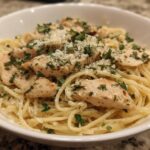 Close-up of a white bowl filled with Light Garlic Chicken Pasta, topped with sliced chicken, grated cheese, and fresh parsley.
