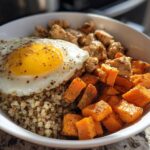 A Meal Prep Breakfast Bowl with protein chunks, roasted sweet potatoes, quinoa, and a sunny-side-up egg.
