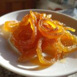 Close-up of glistening, curled strands of Mixed Peel with Vanilla Syrup served in a small white dish.