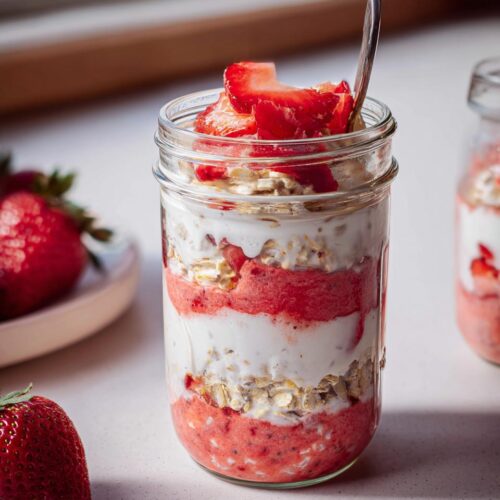 Layers of oats, creamy yogurt, and strawberry puree in a glass jar for No-Sugar Strawberry Cheesecake Overnight Oats.