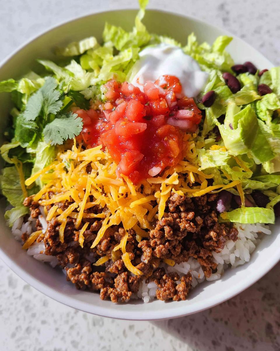 Close-up of a One-Bowl Taco Dinner served over rice with seasoned beef, cheese, lettuce, salsa, and sour cream.
