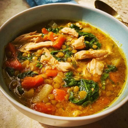 Close-up of a bowl of One-Pot High Protein Soup featuring shredded chicken, green lentils, carrots, and spinach.