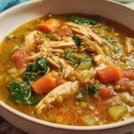 Close-up of a bowl filled with One-Pot High Protein Soup featuring shredded chicken, lentils, carrots, and spinach.