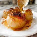 Close-up of caramelized Oven-Baked Onion Boil being drizzled with a sweet glaze from a spoon.