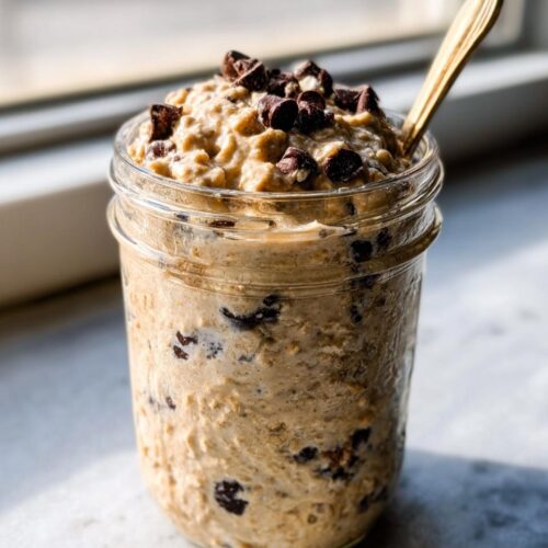 Close-up of Protein Cookie Dough Overnight Oats topped with chocolate chunks in a glass mason jar.