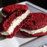 Close-up of Red Velvet Sandwich Cookies with thick cream cheese filling, one cookie broken open.