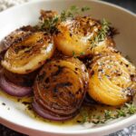 Close-up of caramelized Roasted Onions with Thyme, glistening in pan juices and garnished with fresh thyme sprigs.