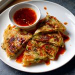Four triangular pieces of golden brown Scallion Pancakes drizzled with chili oil, served with a side dipping sauce.