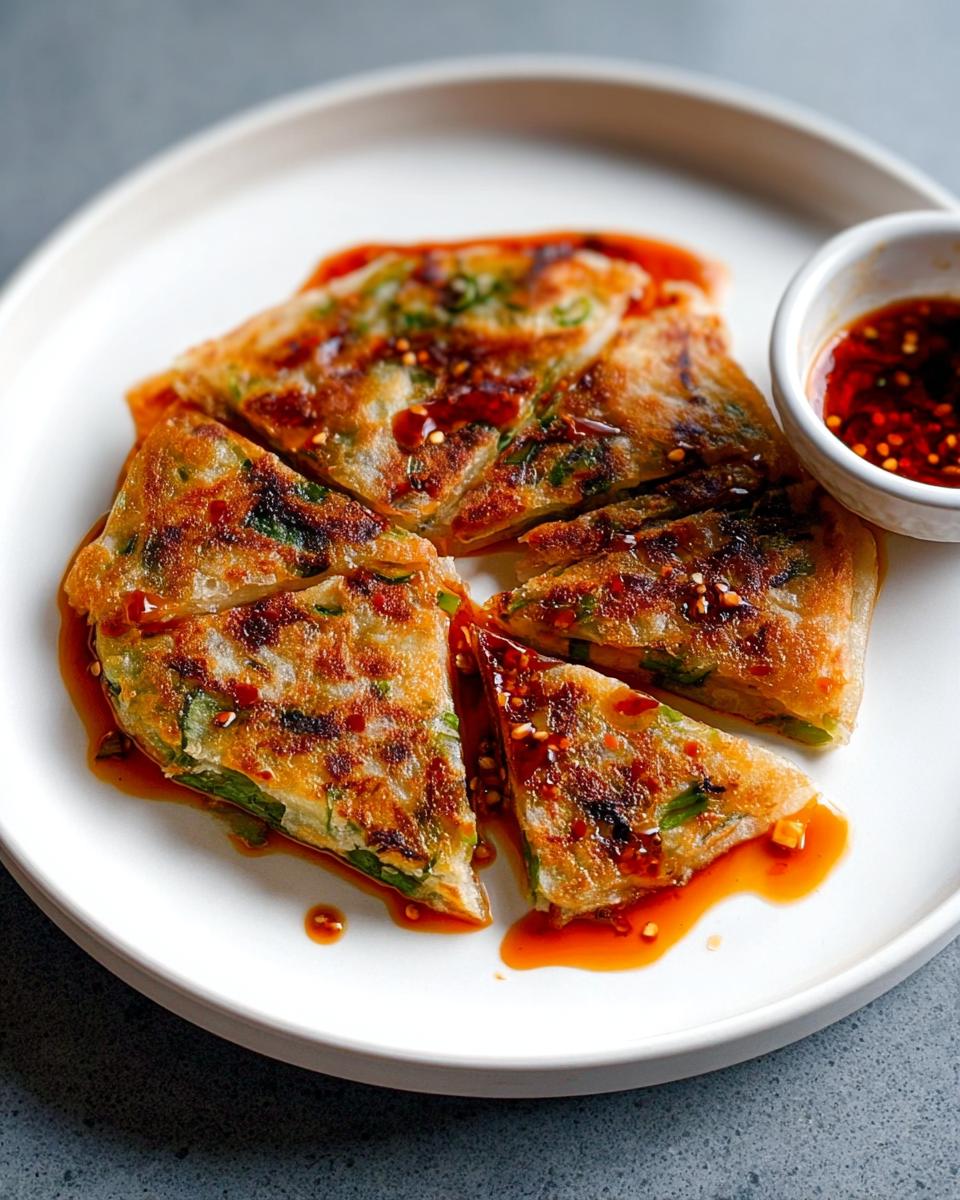 Four triangular slices of golden-brown Scallion Pancakes drizzled with bright red chili oil, served on a white plate.