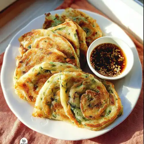 A plate of golden-brown Scallion Pancakes with Sesame Oil, served with a small bowl of dark dipping sauce topped with sesame seeds.