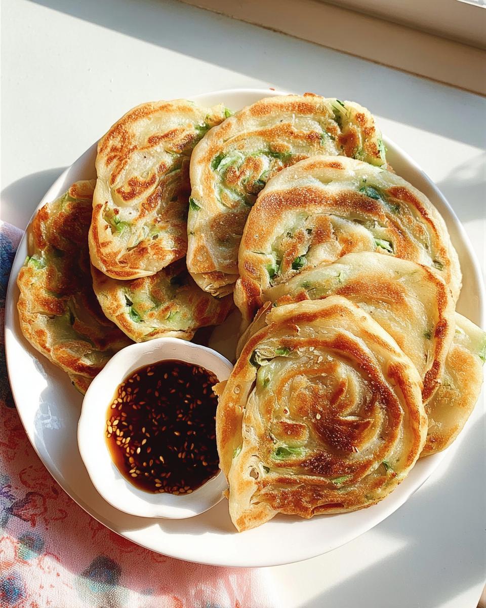 A plate of flaky Scallion Pancakes with Sesame Oil served with a small bowl of dark dipping sauce.