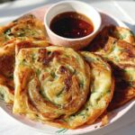 A plate of golden brown Scallion Pancakes with Sesame Oil served with a small bowl of dark dipping sauce.