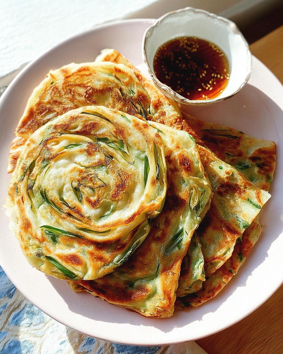A plate of crispy, golden-brown Scallion Pancakes with Sesame Oil dipping sauce on the side.
