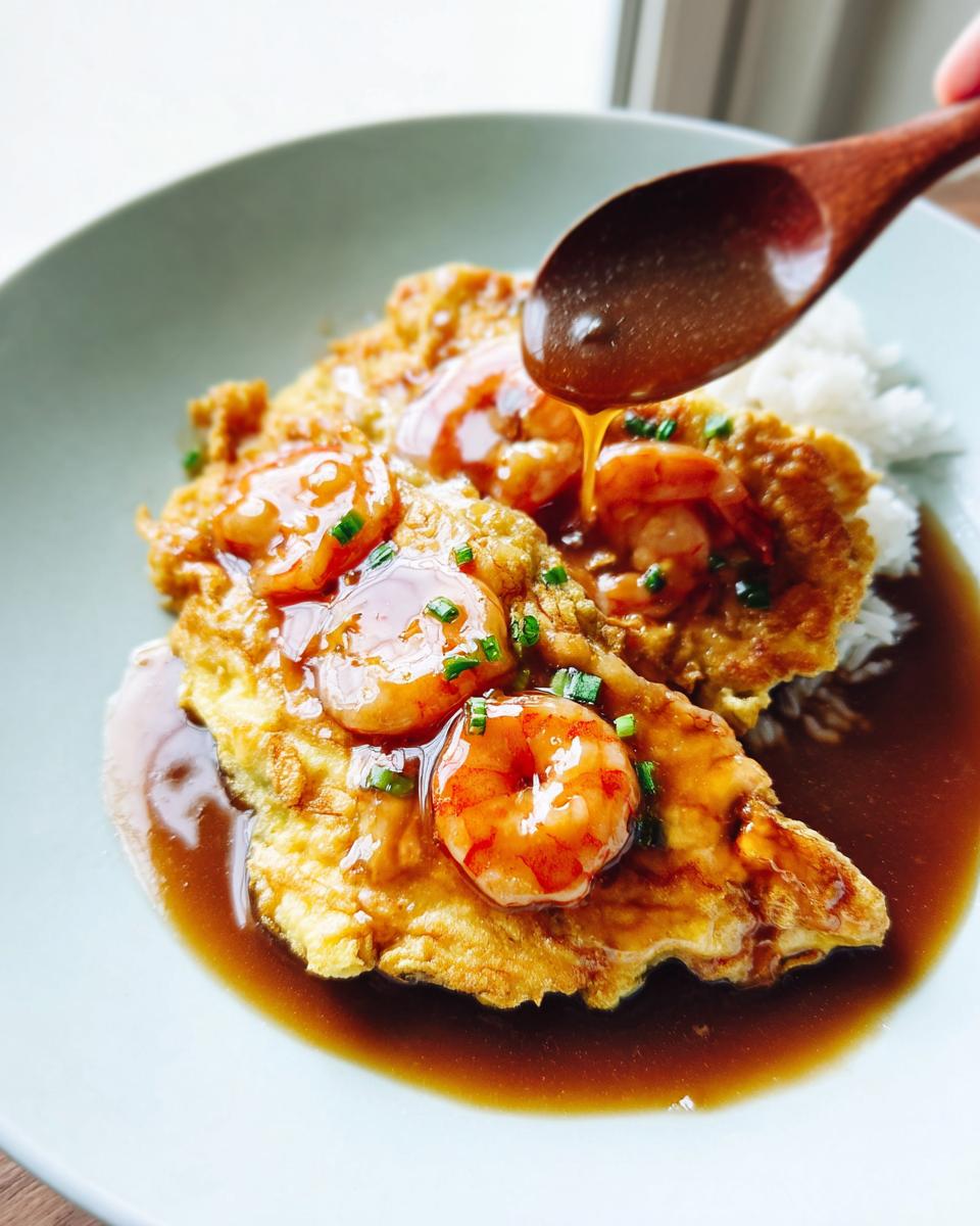 A wooden spoon pours light soy gravy over Shrimp Egg Foo Young served on white rice.