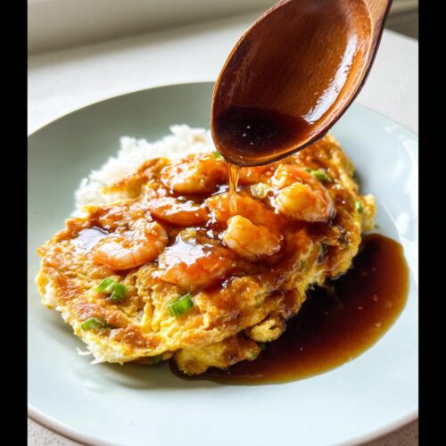 A wooden spoon pours light soy gravy over Shrimp Egg Foo Young served with white rice.