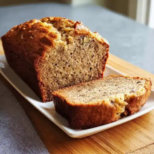 A golden-brown Sour Cream Banana Cake Loaf, partially sliced on a white platter.