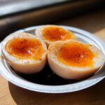 Three halves of soft-boiled Soy Sauce Boiled Eggs with jammy orange yolks, sitting in dark marinade.
