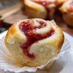 A close-up of a soft, golden Strawberry Cheesecake Roll topped with a swirl of bright red strawberry jam.
