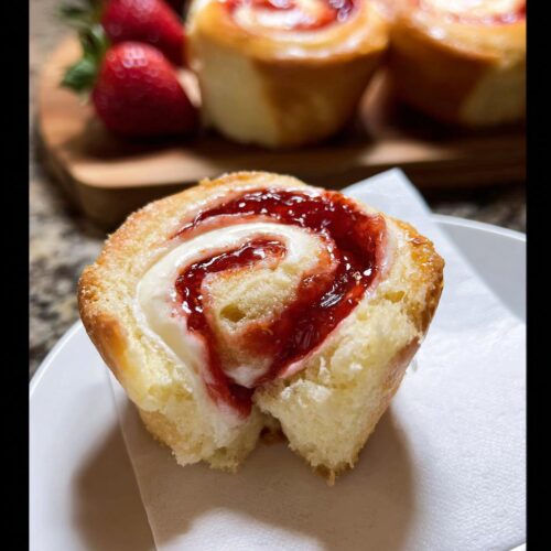 A close-up of a soft Strawberry Cheesecake Roll, broken open to show the creamy filling swirled with bright red Strawberry Jam.