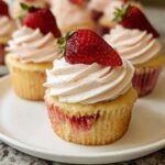 Close-up of a Strawberry Valentine Cupcake with pink whipped frosting and a fresh strawberry on top.