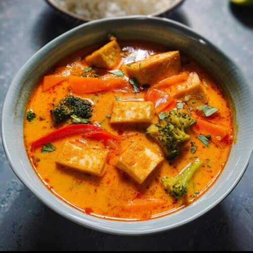 Close-up of a vibrant bowl of Thai Red Curry Soup with Tofu, broccoli, and carrots in a rich orange broth.