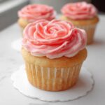 Close-up of a vanilla cupcake topped with vibrant pink buttercream shaped like a rose, part of a batch of Valentine Cupcakes.